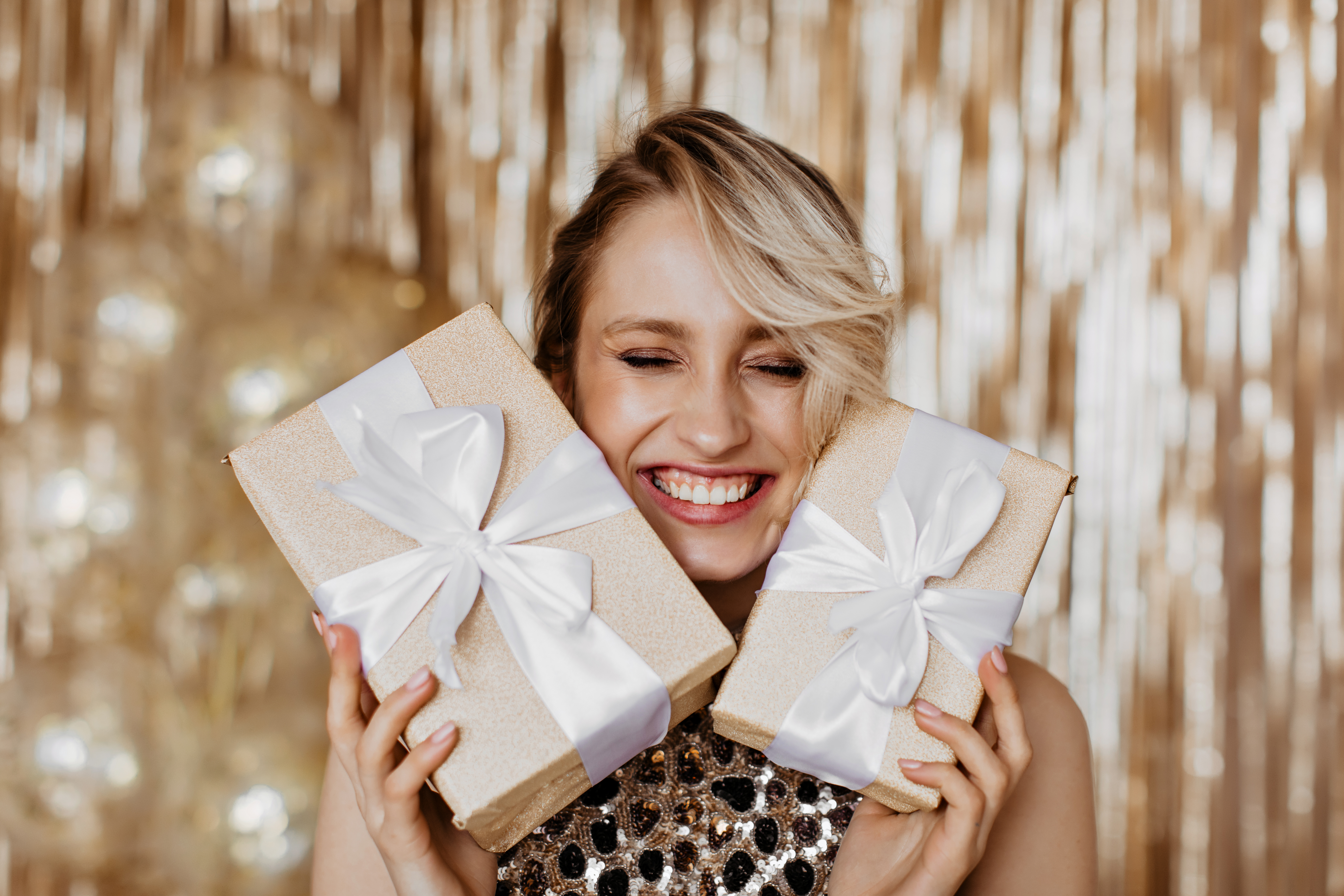 Blonde girl sincerely rejoices at gifts received and laughs on golden background